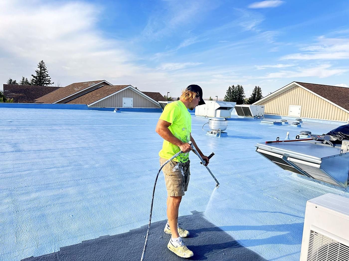 Revive crew member spraying roof coating on a commercial building