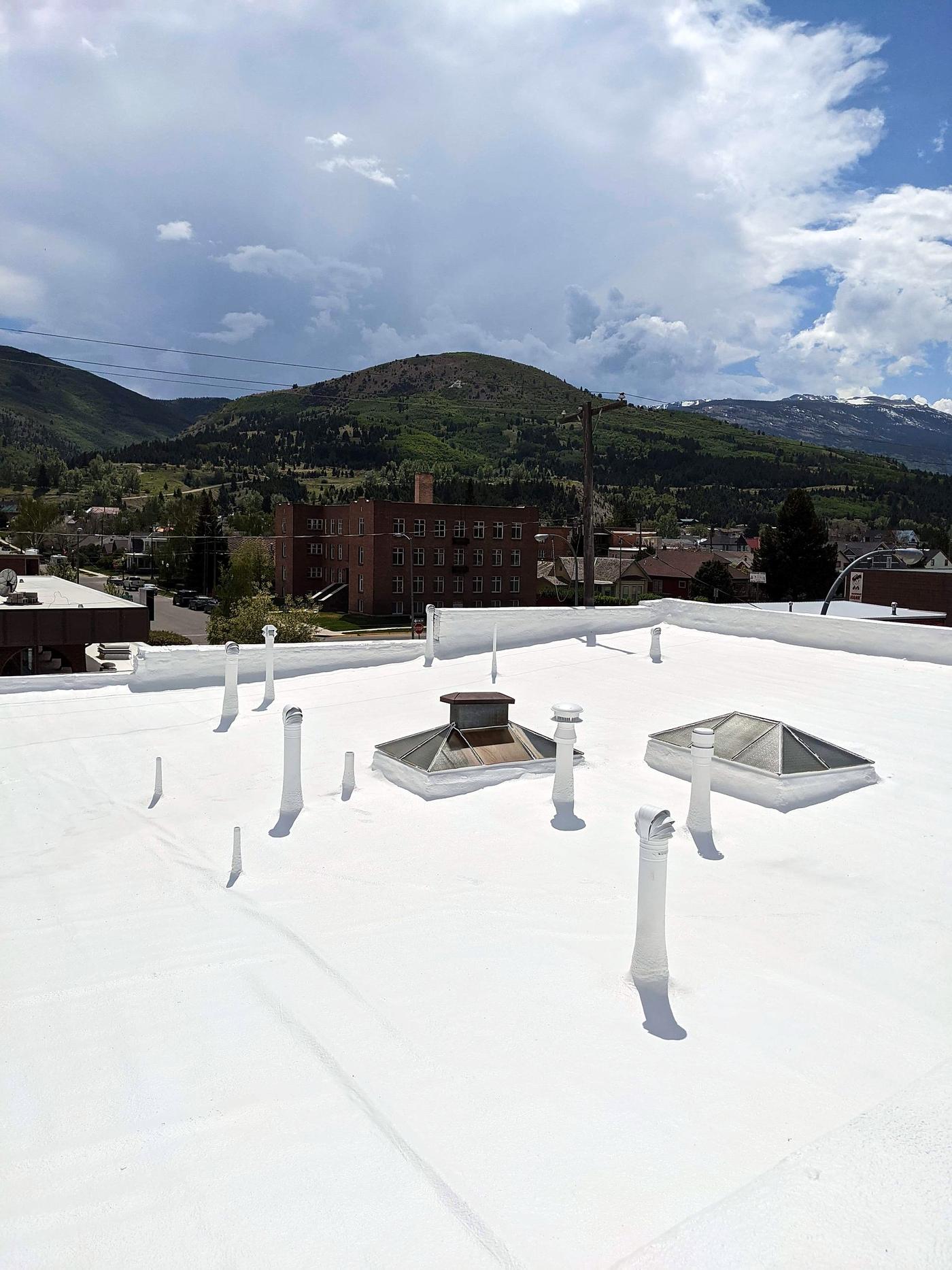 Finished white roof coating on a flat commercial roof, with mountains in the background