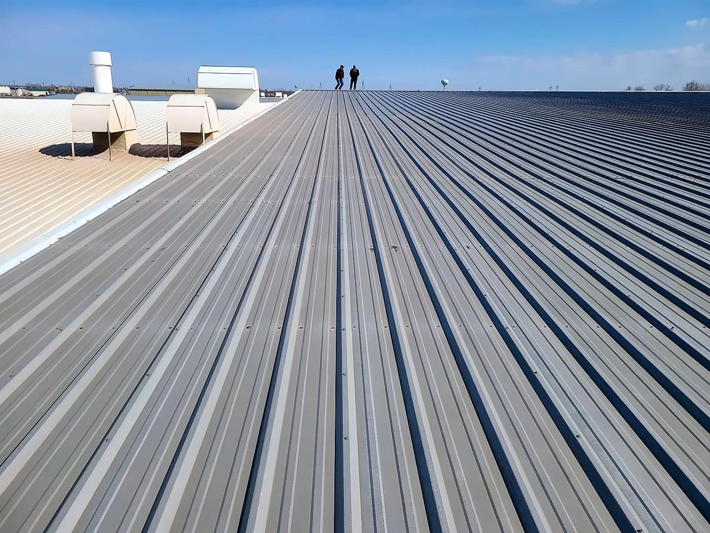 Two people walking a long ribbed metal roof during an inspection