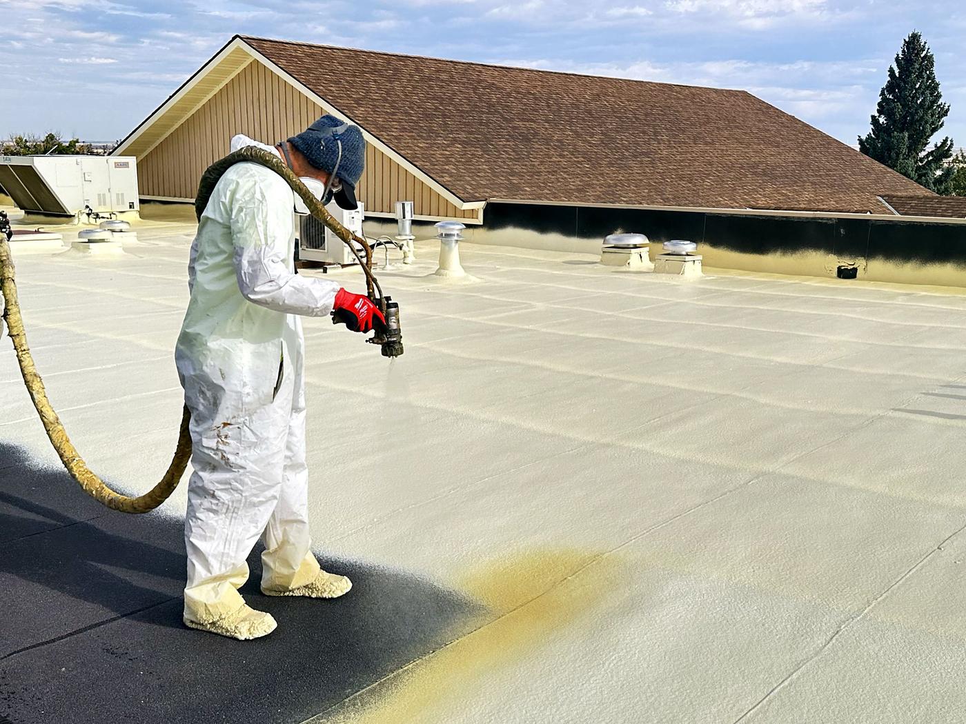 Crew member in a protective suit spray-applying roof coating